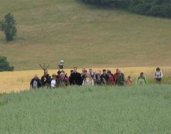 Gruppe von Menschen/Pilgern zieht durch Felder und Wiesen