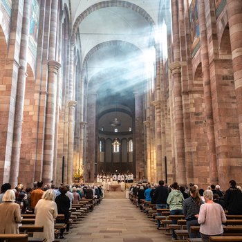 Blick von hinten in Richtung Altar während des Gottesdienstes, links und rechts stehen Menschen in den Bänken, vorne am Altar steht der Bischof