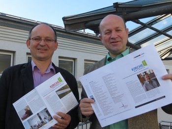 Ökumenische Öffentlichkeitsarbeit Zwei Verantwortliche halten je eine katholische und eine protestantische Ausgabe des einheitlichen Pfarrbriefs in Händen