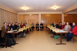 Menschen sitzen an einem zum Hufeisen aufgestellten langen Tischen.