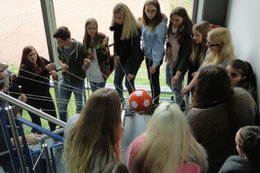 Junge Menschen stehen in einem Treppenhaus und haben in ihren Händen ein Netzt aus Fäden, in der Mitte des Netzes liegt ein roter Ball mit weißen Punkten.