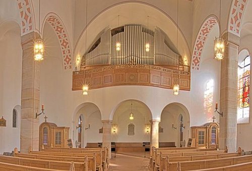 Blick in Kircheninnenraum, vorne Sitzbänke, dahinter der Altarraum, darüber die Orgel.