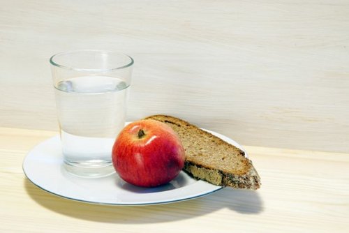 Teller mit einem Glas Wasser, einem Apfel und einem Stück Brot.