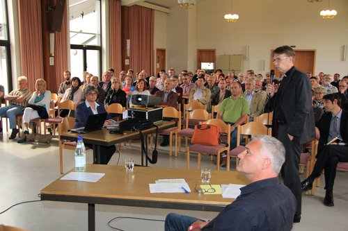 Eine Gruppe von engagierten Frauen und Männern aus Pfarreien sitzen in einem Saal und hören den Erklärungen von Domkapitular Schappert zu.