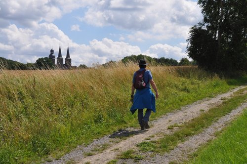 Mann wandert auf einem Feldweg durch grüne Felder